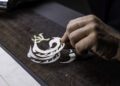 A hand meticulously applies a bespoke Phantom Dragon stencil design onto a wooden surface.