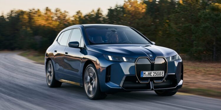 A blue BMW electric SUV driving on a road with blurred background trees.