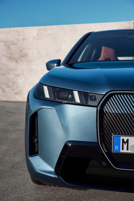 Close-up of the front view of a modern blue car with sleek headlights and a distinctive grille, parked outdoors.