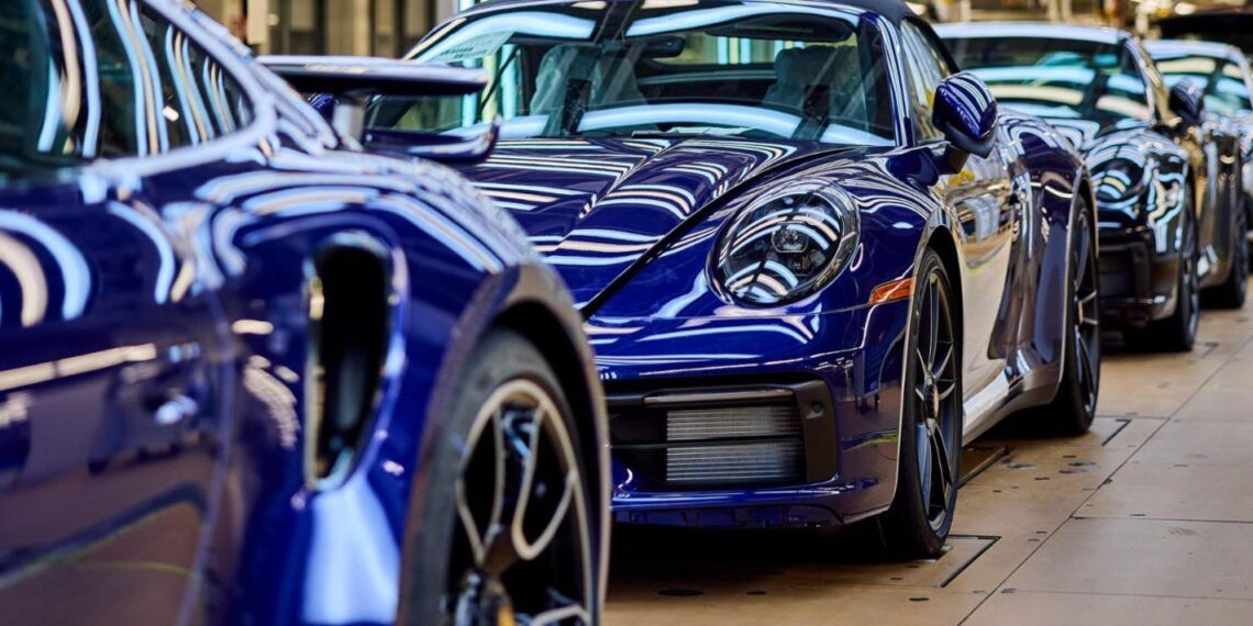 A line of sleek blue sports cars, resembling Porsche models known for record sales in the U.S., gleams in the factory setting with prominent reflections and elegant design.