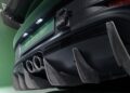 A close-up of the rear of a Porsche 911 GT3 RS showcases dual exhaust pipes, a prominent diffuser, and a partially visible license plate, all set against a lush green backdrop.