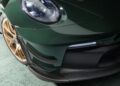 Close-up of a green Porsche 911 GT3 RS, highlighting its front headlight, air vent, and gold wheel on a concrete floor.