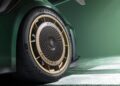Close-up of a car wheel with gold rim, showcasing "Porsche" and "MANTHEY" text, on a 911 GT2 RS Manthey Kit. The black tire complements the dark green body under the softly lit background.