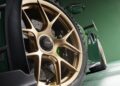 Close-up of a Porsche 911 GT3 RS sports car showcasing its bronze alloy wheels and visible rear spoiler, set against a lush green background in the U.S.