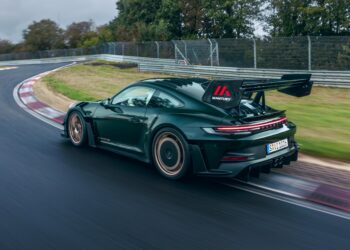 A dark green Porsche 911 GT3 RS roars down a wet U.S. racetrack, leaving a blur of trees in its wake.
