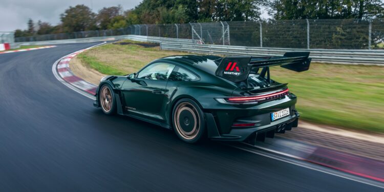 A dark green Porsche 911 GT3 RS roars down a wet U.S. racetrack, leaving a blur of trees in its wake.