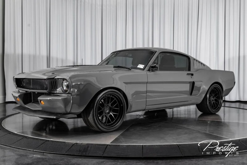 A sleek gray vintage Ford Mustang, a unique creation, stands proudly on display in a showroom with a white curtain backdrop.