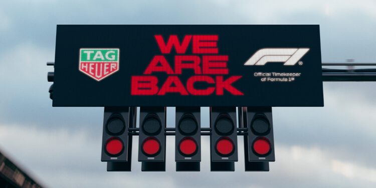 A Formula 1 starting light proudly flashes "WE ARE BACK," accompanied by the iconic TAG Heuer emblem, celebrating its role as the Official Timekeeper alongside the F1 logo.