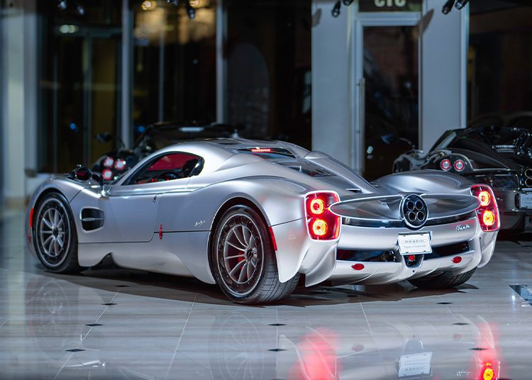 A sleek silver sports car from Miller Motorcars, with a modern design, gleams under the lights as it sits parked indoors on a shiny tiled floor. The Pagani Utopia awaits its new owner, exuding elegance and performance in every curve.