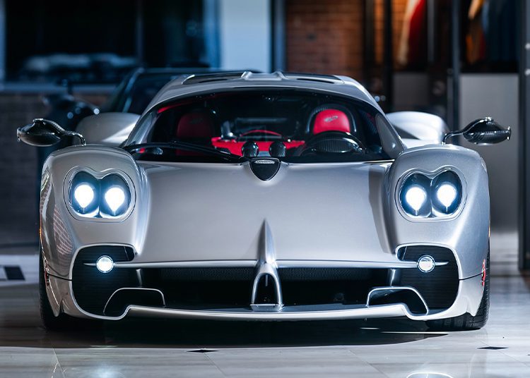 A stunning silver Pagani Utopia with illuminated headlights, sleek aerodynamic design, and a luxurious red interior awaits its new owner at Miller Motorcars' indoor showroom.