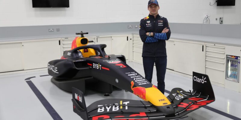 A person stands next to a Red Bull Formula 1 car in a garage, embodying the pinnacle of luxury and lifestyle within the high-octane world of motorsports.