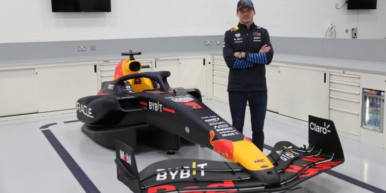 A person stands next to a Red Bull Racing car in a garage, where the dark color scheme and prominent Red Bull logo shine. The scene evokes the thrill of a Red Bull F1 Simulator, capturing the essence of Max Verstappen's legendary racing spirit for charity enthusiasts.