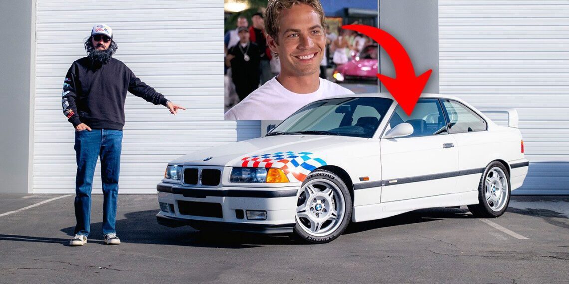 A person stands next to a white E36 BMW M3 Lightweight with a racing flag design. A red arrow points to a photo of another person, possibly Supercar Ron, on the wall behind.