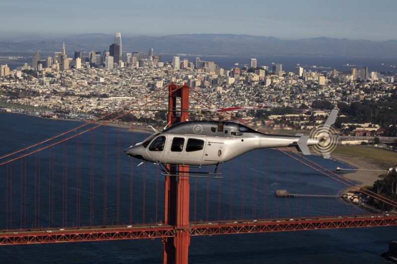 A helicopter from the 2025 duPont REGISTRY edition gracefully flies near the Golden Gate Bridge, with the stunning San Francisco skyline serving as a picturesque backdrop.