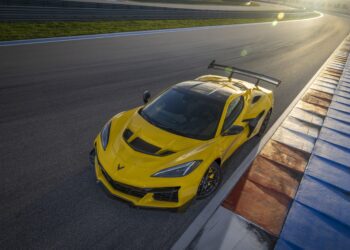 The 2025 Corvette ZR1, boasting a formidable 1,000 HP, glides gracefully around the racetrack. Captured in sunlight with its vivid yellow hue and a sizeable rear spoiler, this Chevrolet masterpiece speeds past a curbed section with unrivaled precision and power.