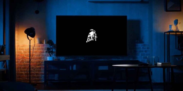 A dimly lit living room features a large Smart TV App displaying a white logo of a bull reminiscent of Lamborghini on a black screen. A floor lamp and assorted furniture are visible, creating an inviting atmosphere for viewers worldwide.