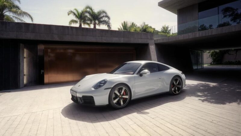 A white sports car parked in front of a modern house with palm trees in the background.