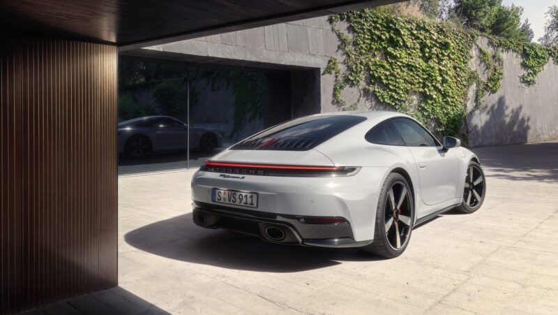 A silver sports car is parked on a concrete driveway next to a modern building with ivy-covered walls.