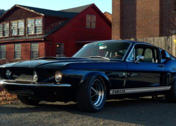 A black Shelby GT350, embodying a true revival of automotive elegance, is parked outdoors with brick buildings in the background, capturing the spirit of Petrolicious style.