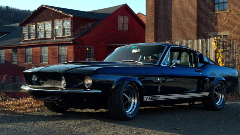 A black Shelby GT350, embodying a true revival of automotive elegance, is parked outdoors with brick buildings in the background, capturing the spirit of Petrolicious style.