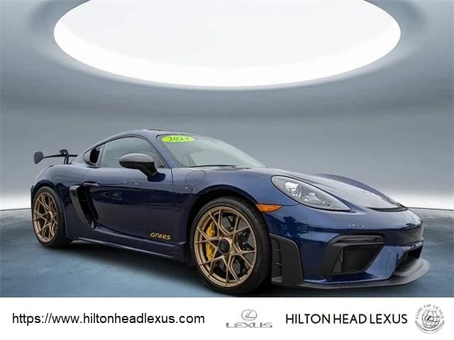 A blue 2022 Porsche 718 Cayman GT4 RS with gold wheels is showcased in a well-lit showroom, featuring Purist Performance branding at the bottom—a standout addition among cars for sale.
