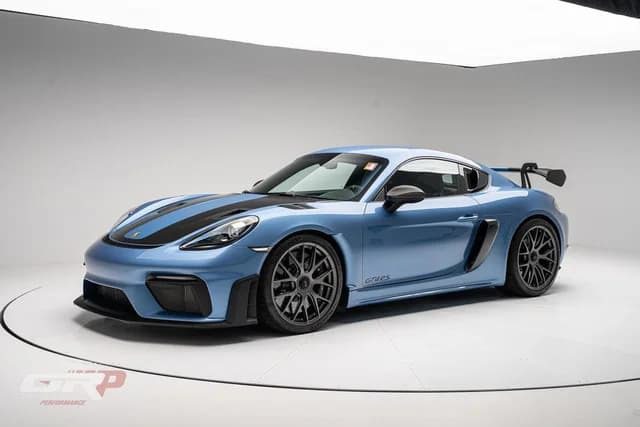 A Porsche 718 Cayman GT4 RS sports car with black accents and a rear wing is displayed in a white studio with minimal background detail, capturing the essence of Purist Performance.