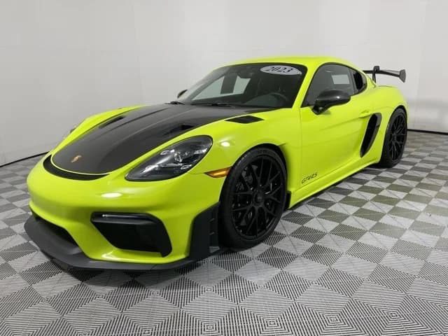 A bright yellow Porsche 718 Cayman GT4 RS with a black hood and rear wing is parked on a checkered showroom floor, showcasing the allure of top-tier performance cars.
