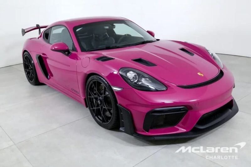 A magenta Porsche 718 Cayman GT4 RS with a rear wing is parked indoors on a light-colored floor. "McLaren Charlotte" is visible in the lower right corner, highlighting Purist Performance and premium cars for sale.