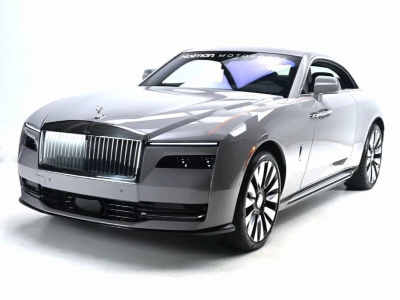 A silver ultra-luxe coupe car with a distinct vertical grille and large alloy wheels, inspired by the Rolls-Royce Spectre electric super coupe, is displayed in a well-lit studio setting.