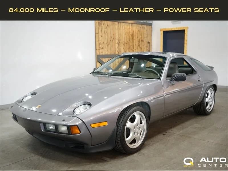 A silver Transaxle Porsche 928 sports car is parked indoors. The display notes 84,000 miles, a moonroof, leather seats, and power seats—an ideal choice for those looking to invest in unsung classics.