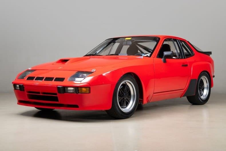 A red Transaxle Porsche 924 sports car is parked indoors on a light-colored floor with a plain gray background—an inviting scene for those looking to invest in unsung classics.