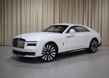 An ultra-luxe Rolls-Royce Spectre electric super coupe is parked indoors on a light-colored floor, framed by elegant beige curtains in the background.