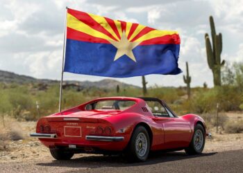 A sleek red sports car adorned with the Arizona state flag is parked on a desert road, cacti and mountains painting the backdrop. Perfect for any duPont REGISTRY feature, this beauty would steal the show at Arizona Car Week 2025.