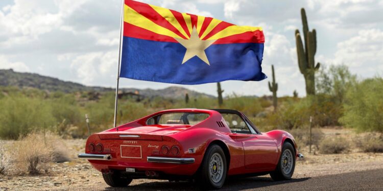 A sleek red sports car adorned with the Arizona state flag is parked on a desert road, cacti and mountains painting the backdrop. Perfect for any duPont REGISTRY feature, this beauty would steal the show at Arizona Car Week 2025.