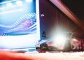 A Porsche Taycan GTS, capable of Guinness World Record-level feats, is parked partly visible on a snowy surface under artificial lighting, next to a building with a glowing sign promoting high performance charging. The scene is reminiscent of its prowess in ice drifting.