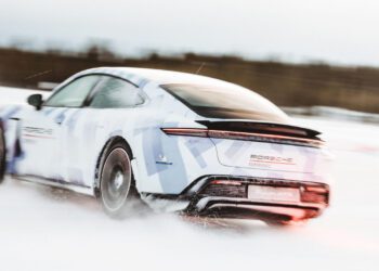 A white Porsche Taycan with blue accents elegantly glides across a snowy surface, creating a slight blur effect. The rear of the car is prominent, showcasing its taillights and logo, as it sets its sights on an epic ice drifting journey worthy of a Guinness World Record.