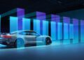 A white Porsche Taycan Turbo GT is parked indoors, with blue and purple light beams projecting in parallel lines around this powerful model.