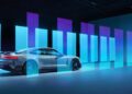 A sleek silver Porsche Taycan Turbo GT is parked indoors, surrounded by vertical, glowing blue and purple light bars, creating a futuristic ambiance that highlights this powerful model.