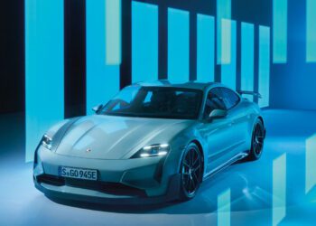 A sleek silver Porsche Taycan Turbo GT is parked in a futuristic setting, accentuated by blue illuminated panels in the background.
