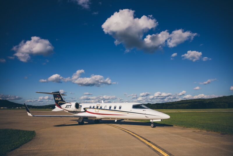 A private jet, featured in the 2025 Aviation Guide by duPont REGISTRY, rests elegantly on a runway under a clear blue sky dotted with scattered clouds.