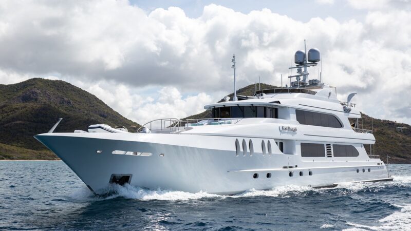 A large, luxury yacht sails gracefully on the water, with a hilly landscape in the background under a cloudy sky, offering an unparalleled maritime experience.