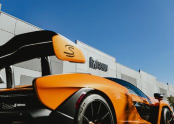 An orange sports car with a prominent rear spoiler is parked in front of a building adorned with "Exclusive Dealer" signage under a clear blue sky, capturing the essence of Jessup, MD.