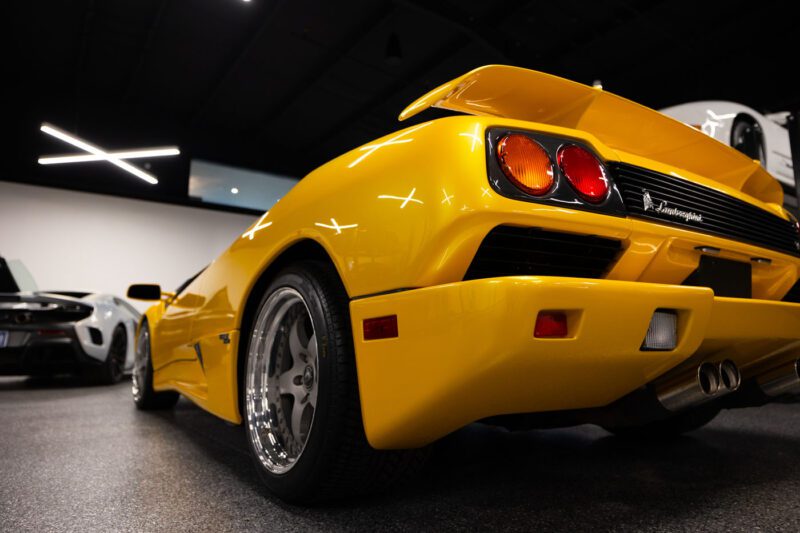 Rear view of a yellow sports car with a spoiler, parked indoors next to other cars at Magden Motors.