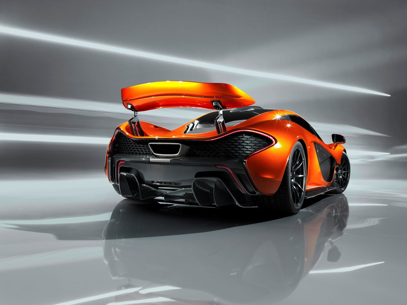 A sleek, orange McLaren P1 sports car with a raised spoiler is shown from the rear against a modern, blurred background.