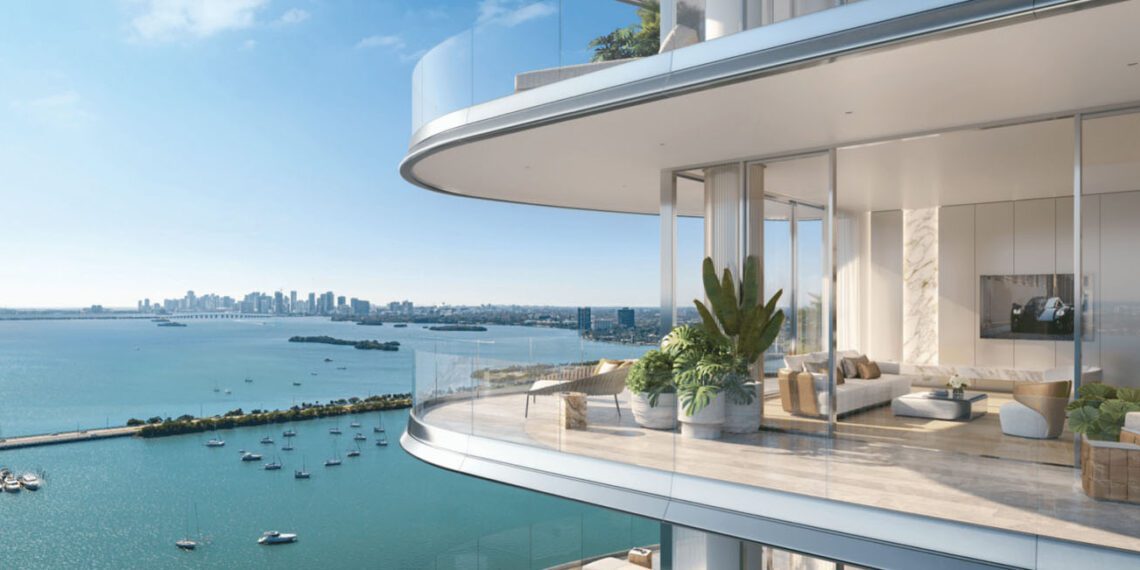 Experience the luxury of a modern high-rise balcony at Pagani Residences, featuring glass railings and breathtaking views of a bay dotted with boats and a distant city skyline. The interior boasts minimalist decor complemented by plants and light furniture, epitomizing sophisticated elegance.