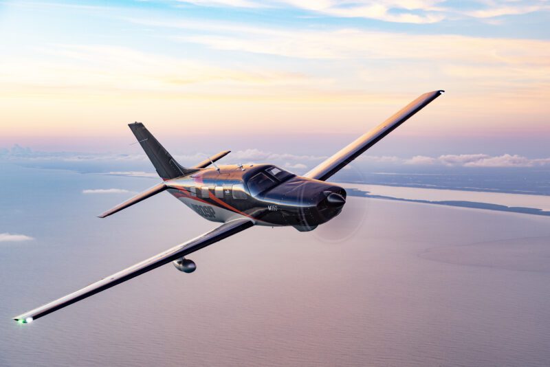 A small propeller airplane from the 2025 duPont REGISTRY glides over the ocean at sunset, offering a breathtaking view of the horizon and clouds, capturing the essence of modern aviation.