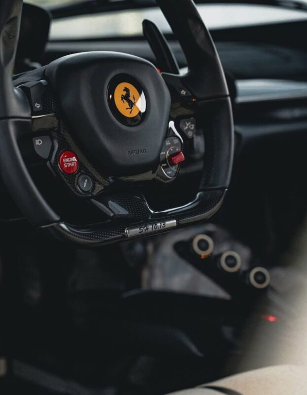 Close-up of a luxury car steering wheel featuring the brand logo, control buttons, and paddle shifters—a masterpiece perfect for any duPont REGISTRY guide or showcase at Arizona Car Week 2025.