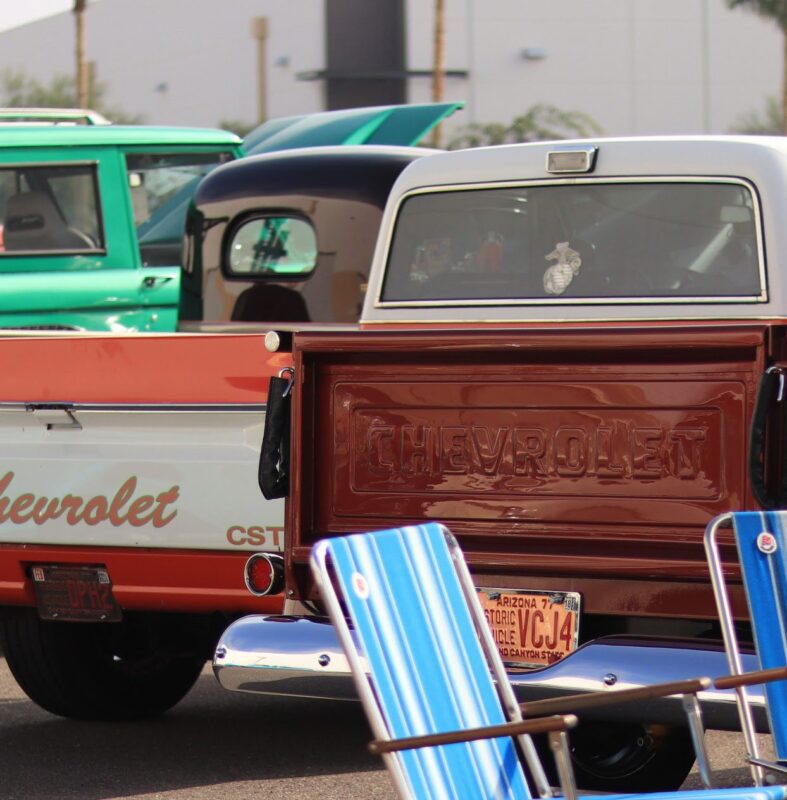 Two vintage Chevrolet trucks, one turquoise and one brown, sit proudly in a parking lot. A striped folding chair adds charm to the scene. This picturesque setting could easily be part of duPont REGISTRY's showcase at Arizona Car Week 2025, where classic beauty meets modern admiration.