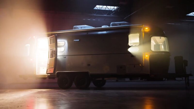 The Airstream trailer, enhanced with the Upgrade Package, stands with its door open, warmly illuminated in the dark like a Midnight Flamingo, creating an inviting glow in the night.
