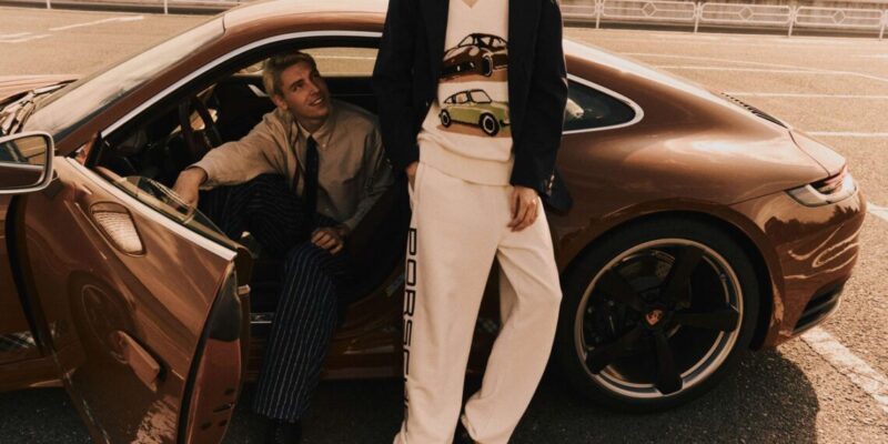 Two people near a parked brown sports car; one is sitting inside, and the other is leaning against it, wearing a sweater with car designs, showcasing a luxurious lifestyle.